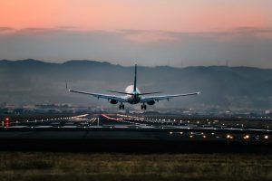 Dramatic view of a commercial airplane landing on a runway at sunset with mountains in the background.